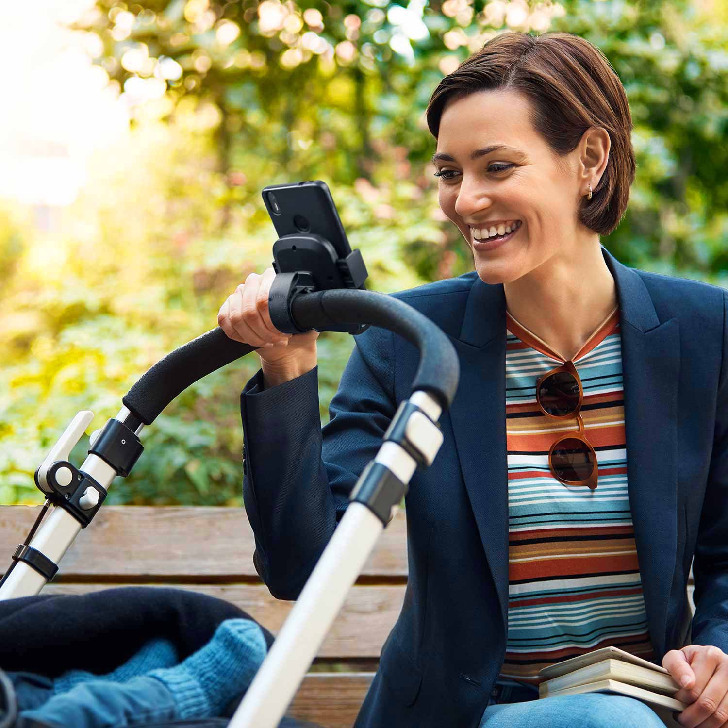 Woman checking the phone installed on the pushchair handlebar.
